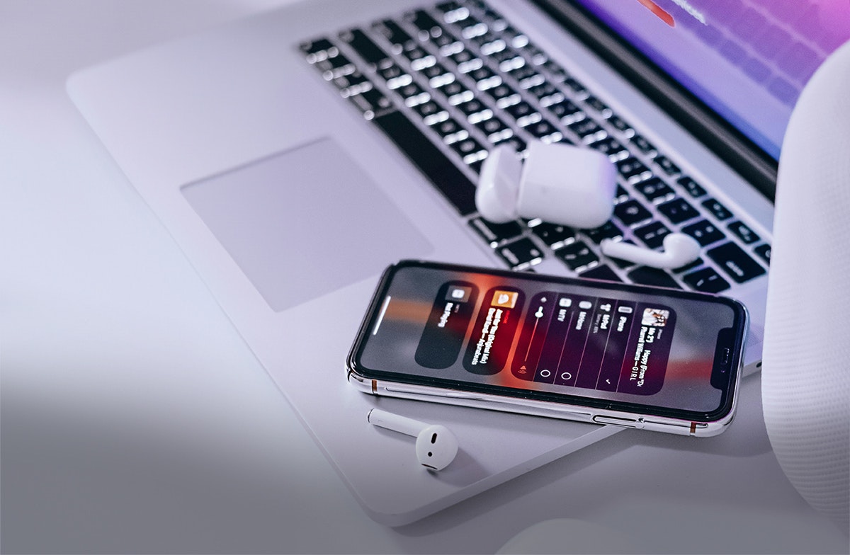 Elektronik Auf einem weißen Tisch liegt ein offener Laptop. Auf dem Rand des Laptops liegen ein Handy und In-Ear-Kopfhörer. In Anlagemetalle sparen mit den Sparplänen von Golden Gates.